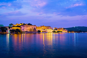 Naklejka premium View of famous romantic luxury Rajasthan indian tourist landmark - Udaipur City Palace in the evening twilight with dramatic sky - panoramic view. Udaipur, India