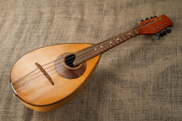 Mandolin located diagonally on a background of rough burlap texture.