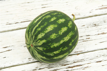 One juicy ripe watermelon berry on a white wooden table background, grown in a greenhouse. I want...