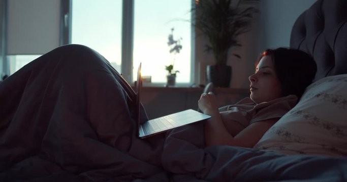 a young girl lying in bed in her bedroom, watching a movie on her laptop and relaxing after a hard day's work.