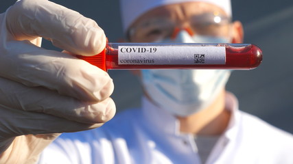 Doctor holding test tube with blood sample to coronavirus. Hand of medic with protective gloves testing blood samples on laboratory. Concept of health and safety life from COVID-19 pandemic. Close up