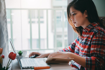 Beautiful asian young woman working from home on laptop computer while sitting at condo living room with confidence posing in coronavirus or covid-19 outbreak situation