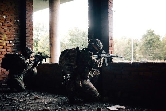 Two military armed soldiers with rifles in their hands shoot at targets while sitting under windows in a building