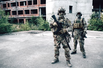 Two armed soldiers in camouflage with rifles on the background of the destroyed building patrolling the city