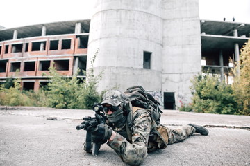 Army soldier lying on the concrete floor in camouflage uniform, aiming at the enemy with a rifle....
