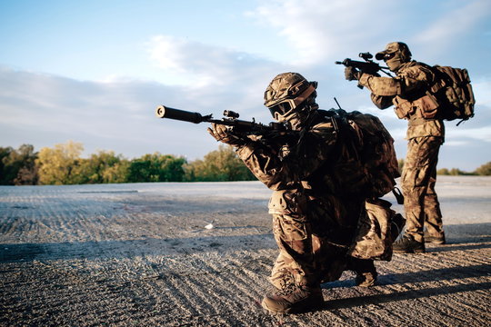 Two soldiers armed with rifles in a shelter aiming at an enemy on the roof of a building