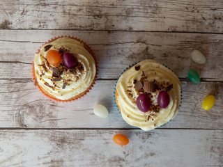Colorful cupcakes decorated with creamy frosting jelly beans and chocolate sprinkles on wooden surface in top view