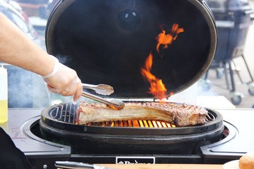 Tomahawk beef steak  with hand on grill with smoke and fire. Cooking process, preparation. Background image, copy space
