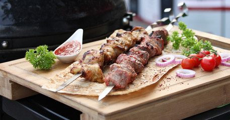 Meat and chicken skewers on pita bread with parsley, onion and cherry tomatoes on a wooden board. Ketchup in a bowl. Picnic. Fried meat on the fire. Background image, copy space