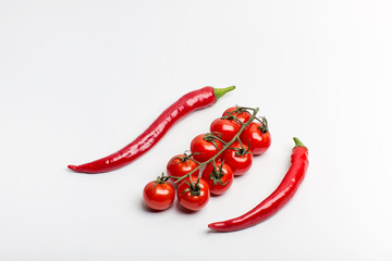 Juicy red hot chili peppers with cherry tomatoes on a branch on a white background