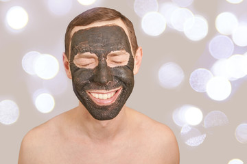 Black Clay Mask on Guy Face. Cosmetology man portrait with mud healthy scrub. Coal nature eco masque. Dermatology mud. Home skin care routine. Skincare male treatment. Pure ecology crack product.