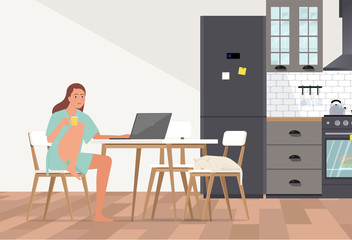 A young woman in a bathrobe with a cup works at a computer in the kitchen.