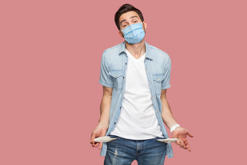 I have no money more. Portrait of sad bankrupt young man with surgical medical mask in blue shirt...