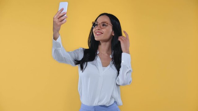 Beautiful smiling businesswoman taking selfie with smartphone isolated on yellow