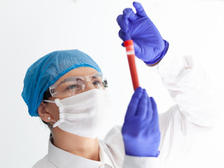 Naklejka premium female doctor in safety glasses, mask and gloves looks at a test tube with blood