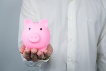 Pink piggy bank in mans hands. Concept of saving and earning money, investments. Copy space.