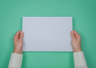 Mans hand hold a sheet of white paper on the green background. Place for a text.