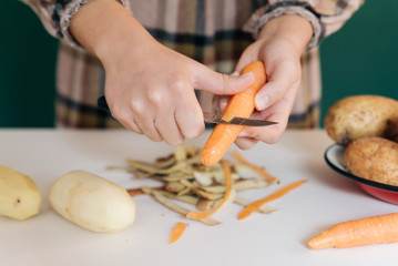 Woman peels off carrots at her kitchen on white marble, to prepare her food.