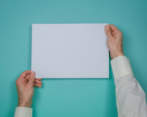 Mans hand hold a sheet of white paper on the blue background. Place for a text.