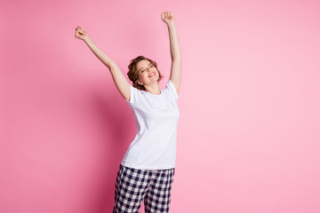 Photo of pretty lady sleepy morning eyes closed enjoy saturday raise hands up stretching wear white t-shirt plaid pajama pants isolated pink color background
