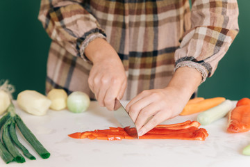 Woman cuts a red pepper at her kitchen on white marble, to prepare her food.