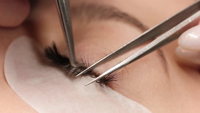 Eyelashes extensions. Fake eyelashes. Eyelash extension procedure.Close up portrait of woman eye with long eyelashes. Professional stylist lengthening female lashes. Master and client in beauty salon.
