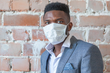 Close up of young African black man in a suit against a red brick wall is afraid of a coronavirus epidemic and wears a medical mask so as not to get infected COVID-19