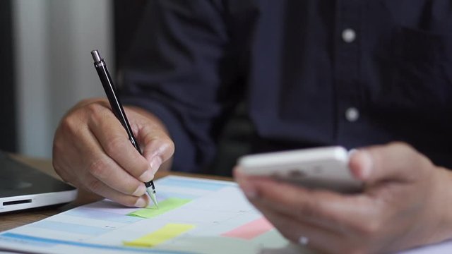 Male hand of planner writing daily appointment On 2023 Calendar book and using smartphone, working space at home.Asian man plan and noted schedule on diary at office desk. Calendar for planner concept