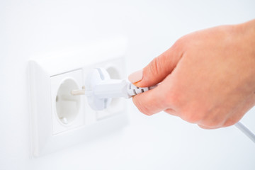 Hand plugging wire into socket on white wall