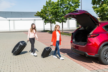 Fototapeta na wymiar Women walk with luggage to car before road trip