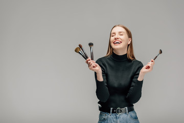 happy makeup artist holding makeup brush set isolated on grey