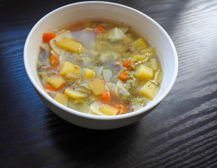 Soup in a white plate of broccoli, carrots, potatoes and square gluten-free pasta . Entree