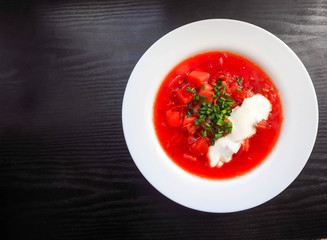 White round plate with soup of national cuisine borscht with sour cream sliced green onion rings on the background of a dark wooden table