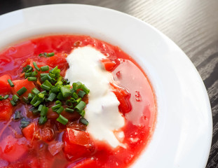 White round plate with soup of Ukrainian national cuisine borscht with sour cream sliced green onion rings