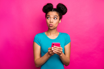 Photo of wondered youngster dark skin lady two buns hold telephone hands look side empty space...