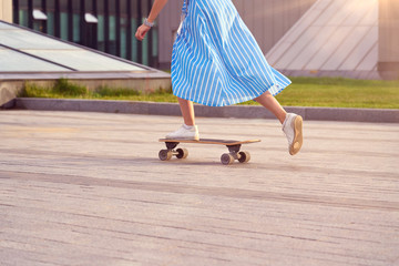 Skater woman in dress is training on longboard, doing a trick outdoor in a public park. Close up on leg kick off.