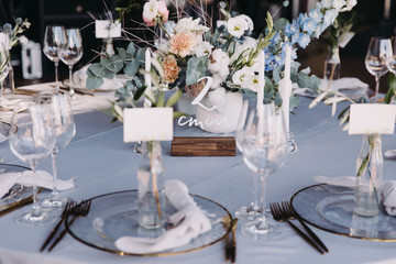 Wedding decor in blue and gray. Banquet tables with tablecloths are decorated with compositions of flowers, on the tables are plates, glasses and candles