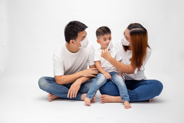Fototapeta na wymiar Asian family wearing protective medical mask for prevent virus Wuhan Covid-19 and sitting together on floor isolated white background. Family protection from contaminated air concept