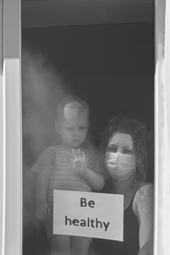 A woman with he son are sitting near a window with the inscription Be healthy, black and white photo.