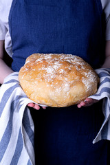 Hot wheat bread in baker's hands against the blue apron
