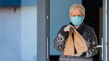 A portrait of an elderly woman in a mask holding food bags. Home delivery in quarantine