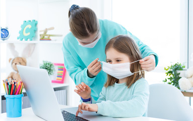 Fototapeta premium Elder sister putting on medical mask on little girl indoors