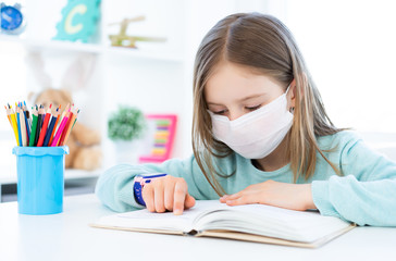 Cute schoolgirl in medical face mask studying at home