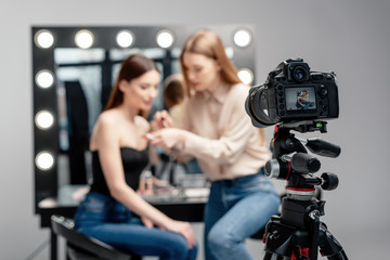 Fototapeta na wymiar selective focus of digital camera near makeup artist holding lip gloss near model isolated on grey