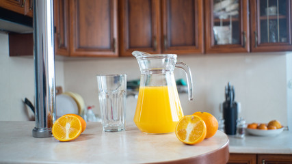 a glass with a decanter stands on a table in the kitchen with orange juice, fresh orange