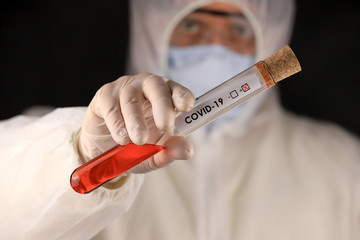 The doctor in a protective suit and mask holding a glass tube with a positive blood test result for...