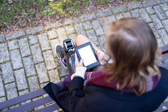 Young woman with leg prosthesis sitting on a bench reading e-book
