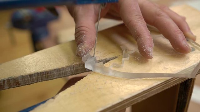 person hand cuts plexiglass with fretsaw holding on special support crafting vintage passenger airplane model close view