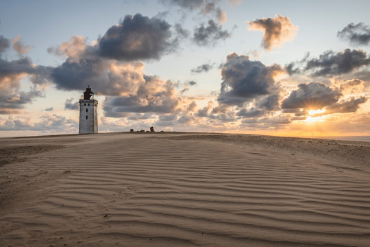 Denmark, Lonstrup, Clouds over rippled sand dunes and Rubjerg Knude Lighthouse at sunset
