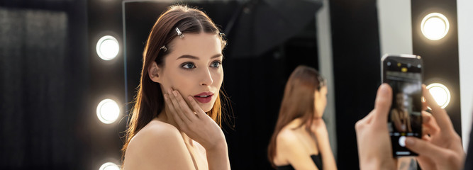 Fototapeta na wymiar panoramic shot of makeup artist taking photo of young model